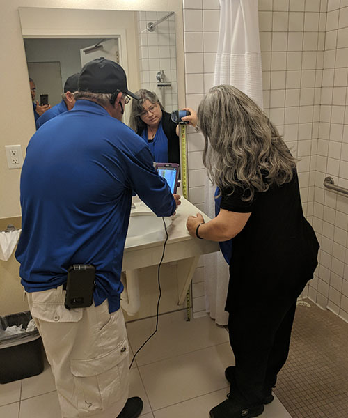 Two Life Quest team members measuring the height of a mirror in a restroom
