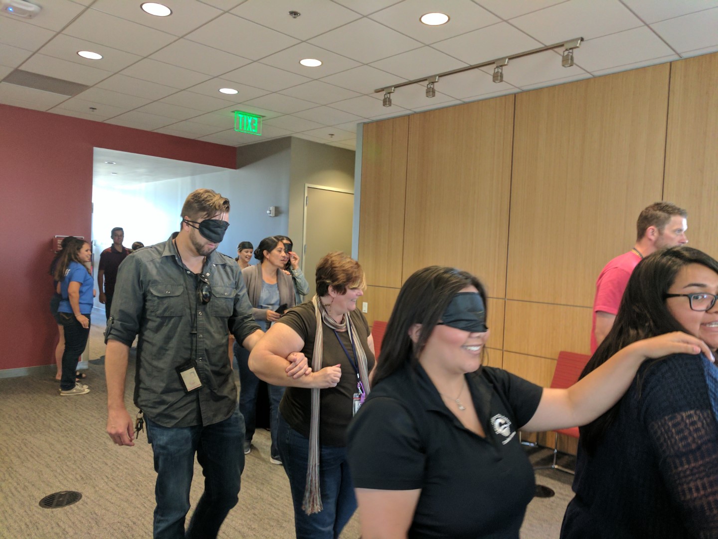 People wearing blindfolds walking side-by-side with people not wearing blindfolds