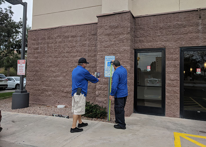 Two Life Quest team members measuring the height of a sign designating accessibility