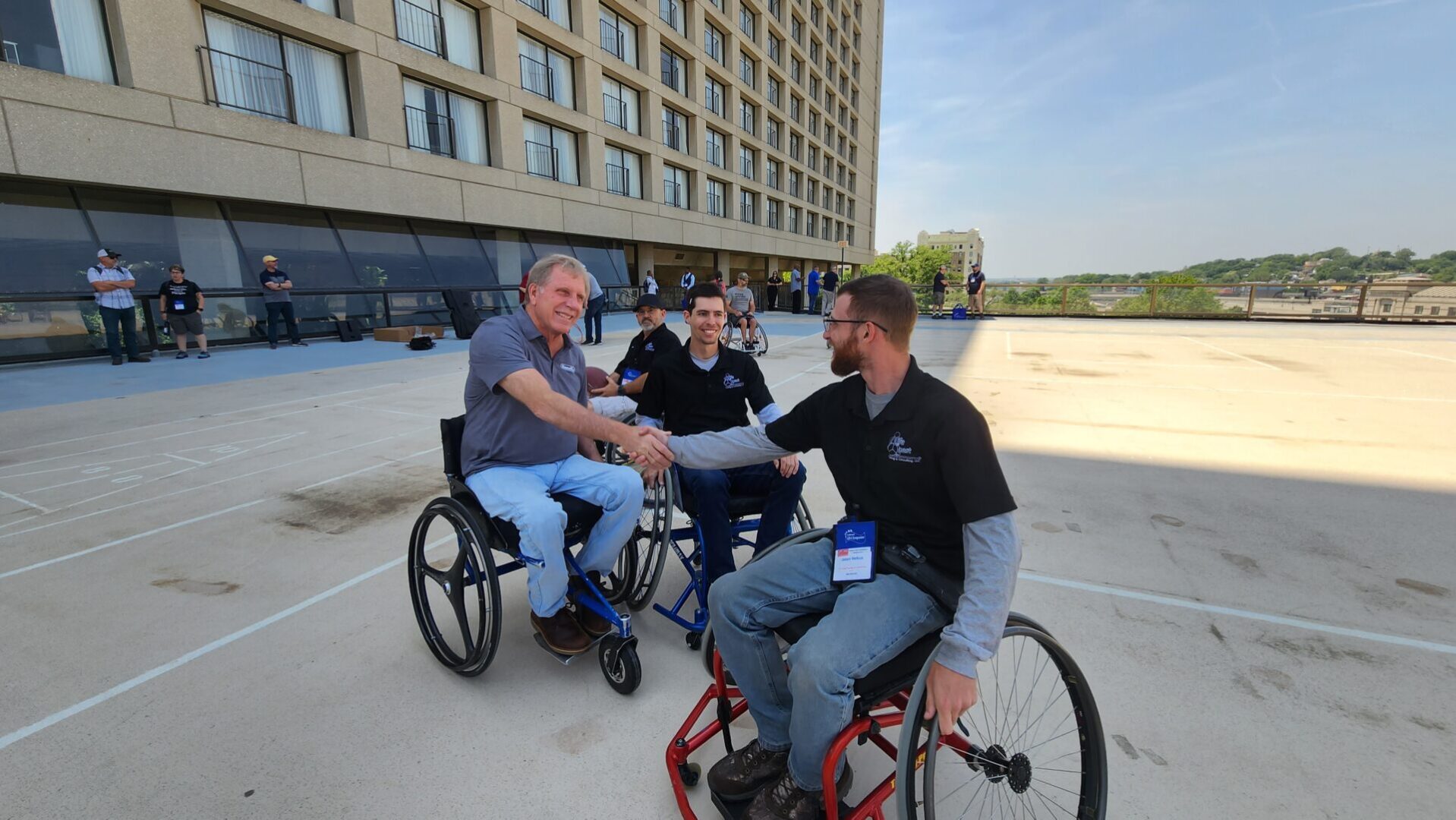 A Life Quest team member shaking hands with Bill Botten, Training Coordinator at the U.S. Access Board. Both individuals are seated in wheelchairs.