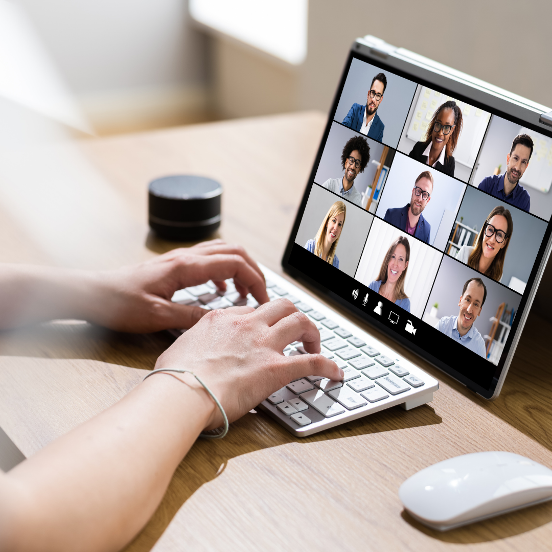 A person typing on a keyboard, participating in a video call with several smiling colleagues.