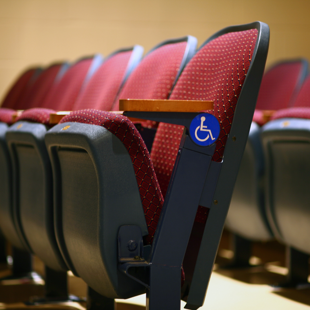 Fixed seating in a small theater. One chair displays the International Symbol of Accessibility.